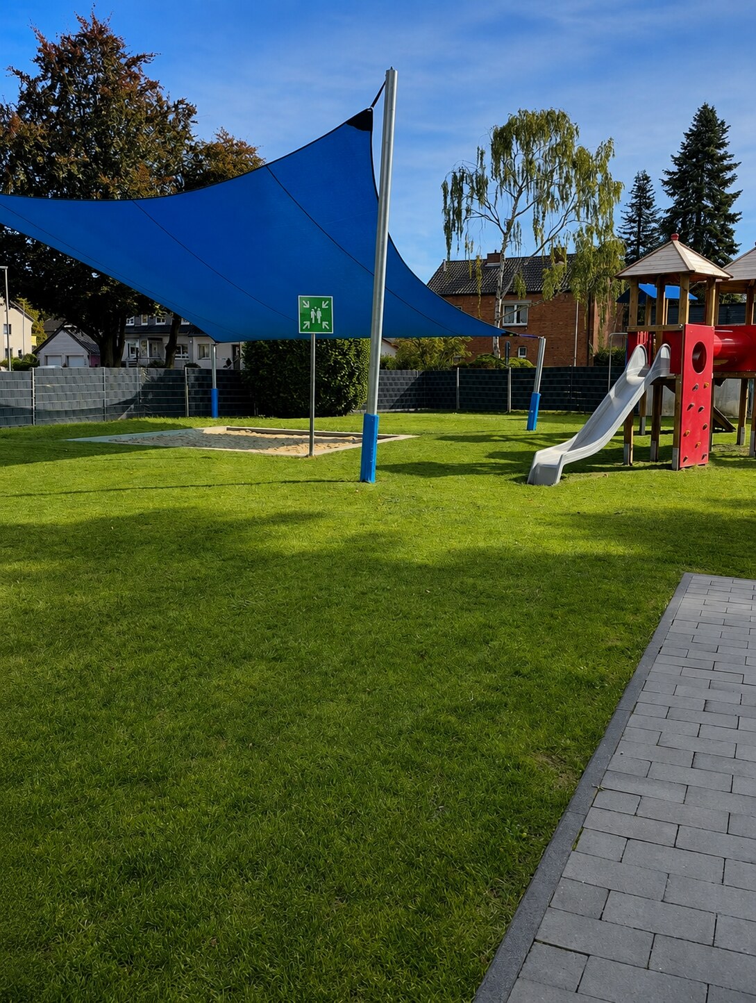 Gepflegte Außenanlage eines betreuten Kindergartens mit blauem Sonnensegel